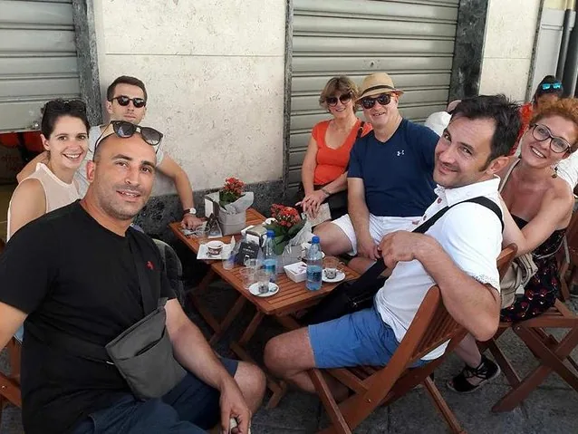 Eine Gruppe lächelnder Touristen sitzt um einen Tisch in einem Straßencafé.