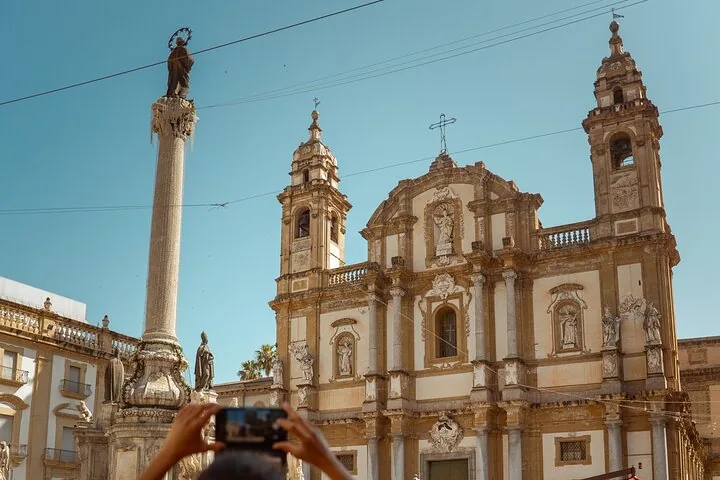 Eine Person fotografiert eine prachtvolle Kirche und eine hohe Säule.